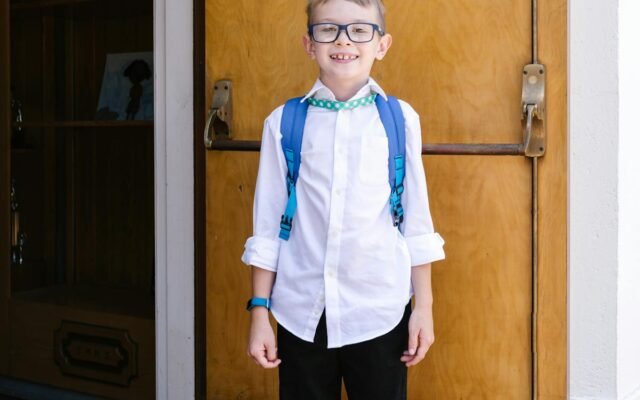Students ar zilu mugursomu stāv pie koka durvīm